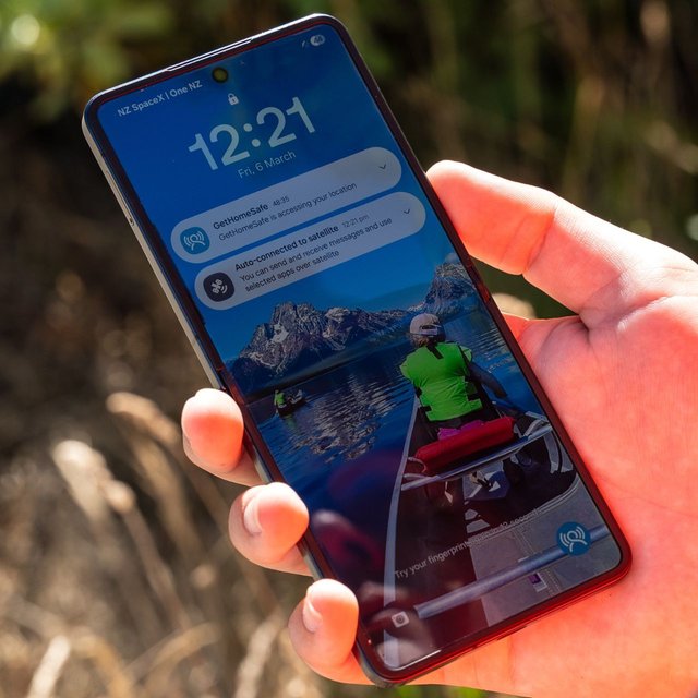 A hand holding a phone showing a GetHomeSafe location notification alongside an auto-connected to satellite alert