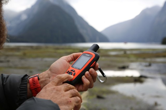 Garmin inReach Explorer Plus satellite communicator held up against a Milford Sound backdrop