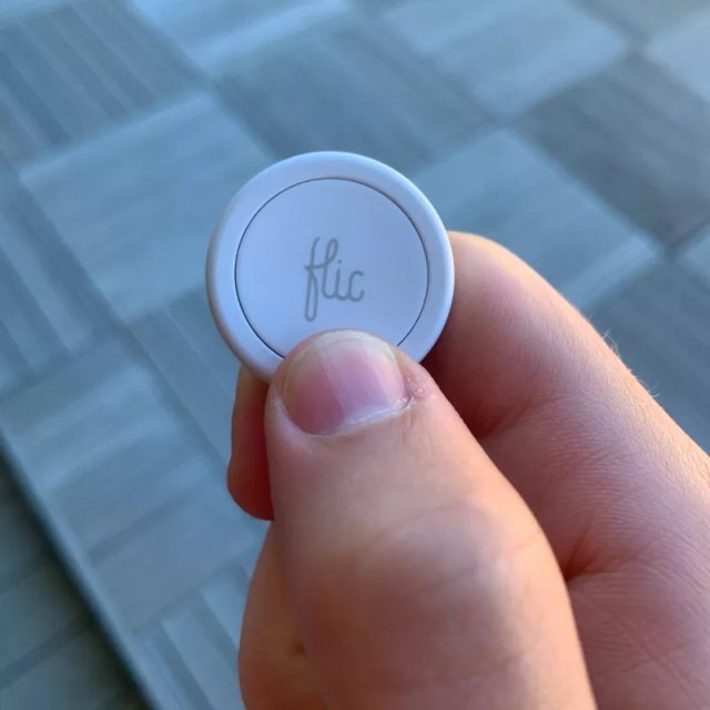 Hand holding a Flic Bluetooth smart button for one-touch check-ins