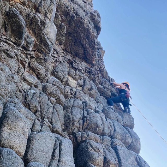 Climber scaling a rocky coastal cliff face at Long Beach Dunedin